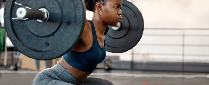 Young woman performing a squat with a barbell in a gym setting, demonstrating strength training techniques relevant to fitness tips.