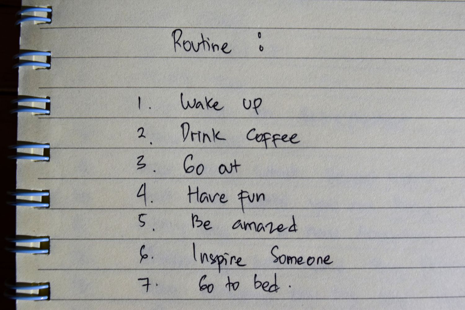 Notebook page titled "Routine" with a handwritten list of daily activities: wake up, drink coffee, go out, have fun, be amazed, inspire someone, go to bed.